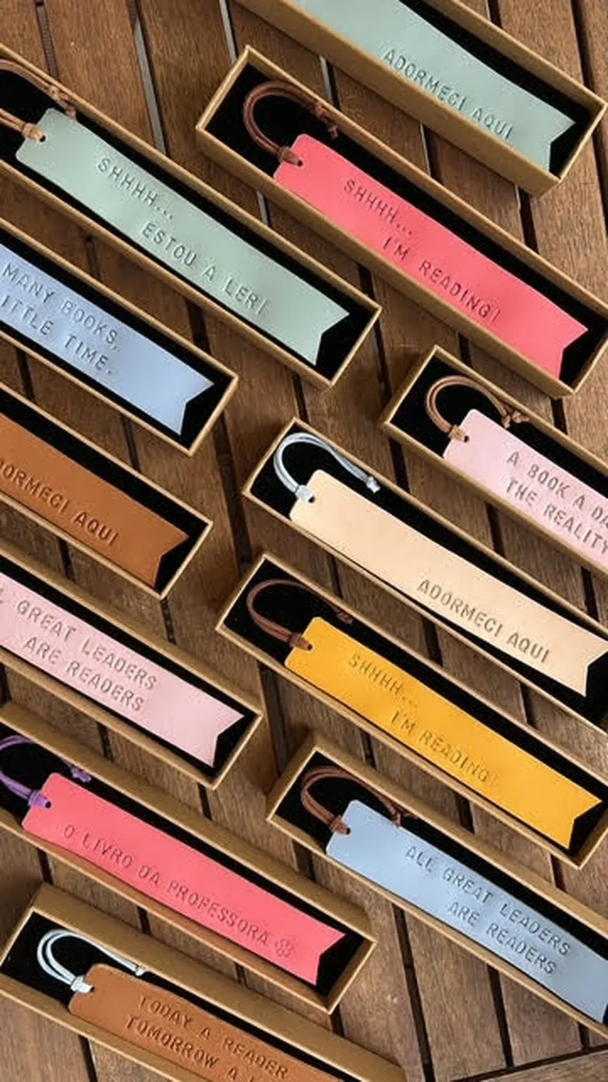 Marcadores de livros em couro de várias cores com frases gravadas, apresentados em caixas individuais.