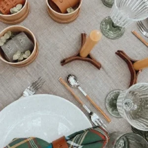 Mesa posta com guardanapos, argolas e candelabros em couro, compondo uma decoração elegante.