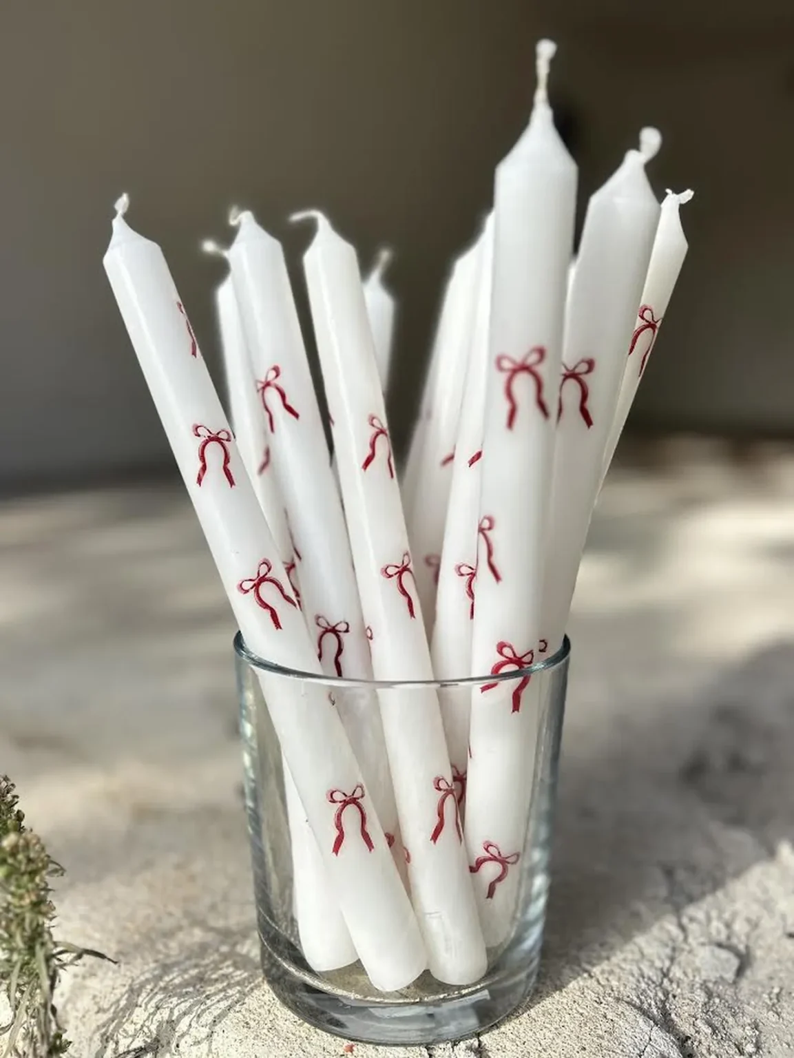 Velas brancas decoradas com laços vermelhos dentro de copo de vidro