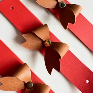 Argolas de guardanapo em couro com laços castanhos sobre tiras vermelhas, com diferentes acabamentos metálicos.