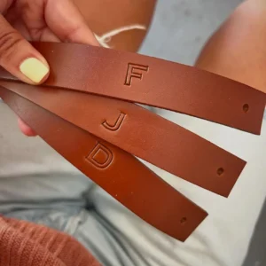 Tiras de couro personalizadas com iniciais gravadas à mão, nas letras F, J e D.