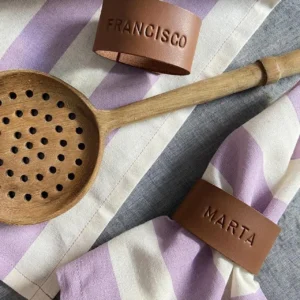 Porta-guardanapos personalizados em pele com os nomes “Francisco” e “Marta”, apresentados sobre guardanapos às riscas lilás e brancas.