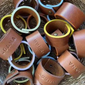 Argolas de guardanapos em couro personalizadas com nomes, em diferentes cores, dentro de um cesto de palha.