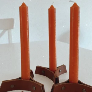 Candelabros artesanais em couro castanho com velas altas laranja.