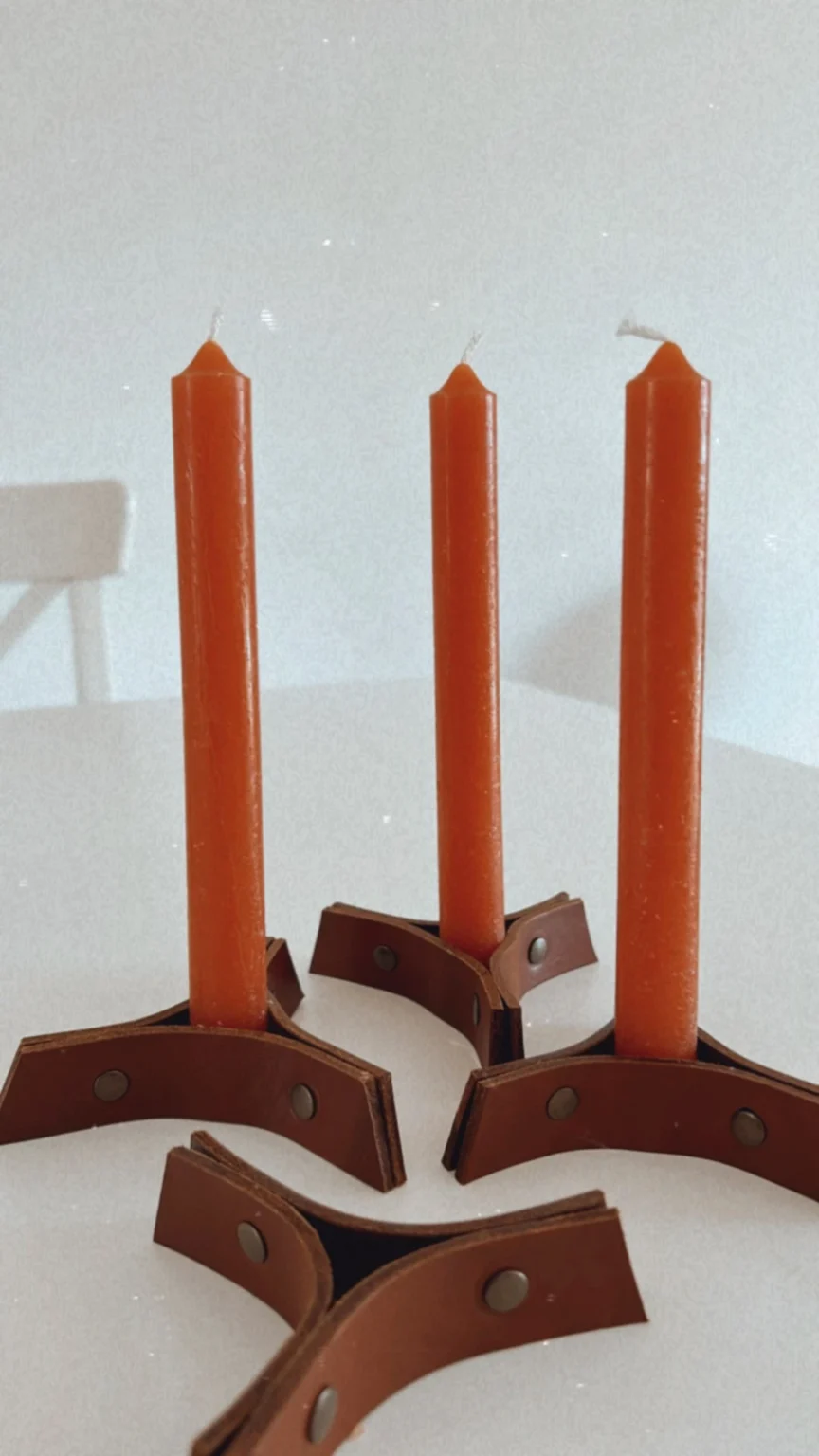 Candelabros artesanais em couro castanho com velas altas laranja.